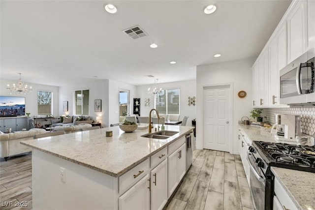 kitchen with sink, white cabinetry, a notable chandelier, stainless steel appliances, and a kitchen island with sink