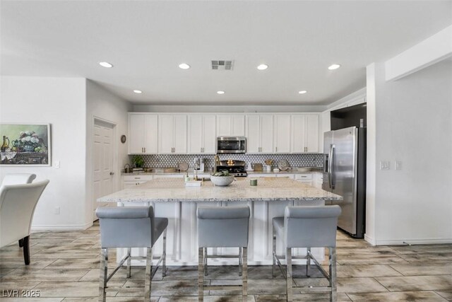 kitchen with white cabinetry, light stone counters, a center island with sink, and appliances with stainless steel finishes