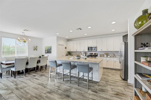 kitchen featuring appliances with stainless steel finishes, decorative light fixtures, tasteful backsplash, white cabinets, and light stone counters