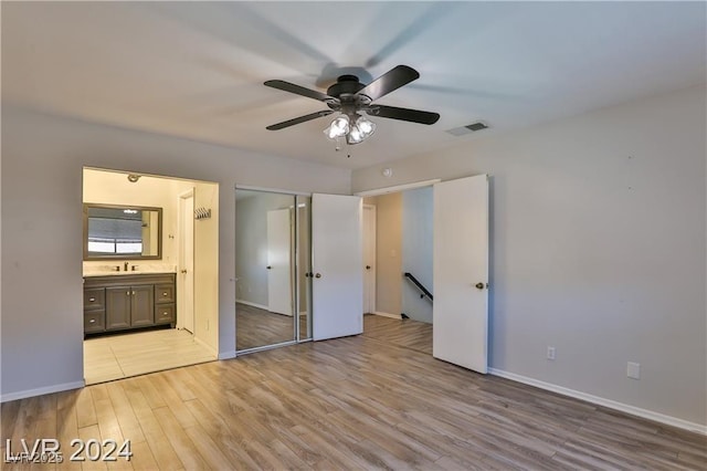 unfurnished bedroom featuring ensuite bathroom, sink, light wood-type flooring, a closet, and ceiling fan