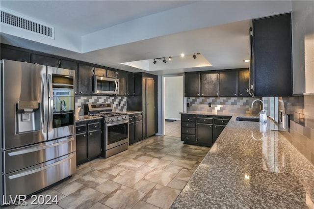 kitchen with sink, stainless steel appliances, a tray ceiling, decorative backsplash, and dark stone counters