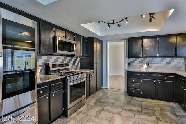 kitchen featuring light stone counters, appliances with stainless steel finishes, a raised ceiling, and backsplash