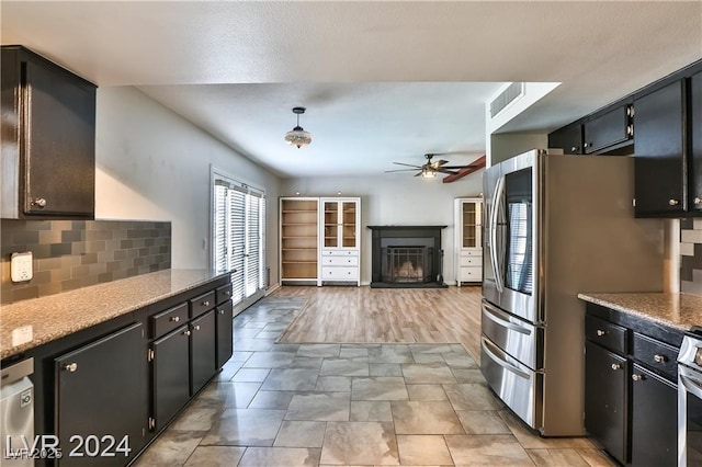 kitchen featuring appliances with stainless steel finishes, pendant lighting, ceiling fan, light stone countertops, and backsplash