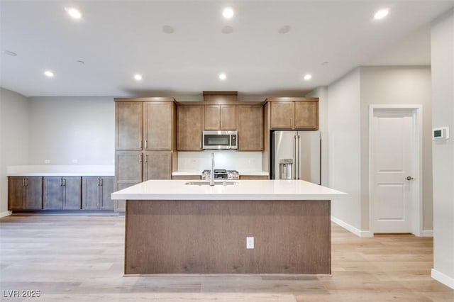 kitchen featuring stainless steel appliances, sink, a center island with sink, and light hardwood / wood-style flooring