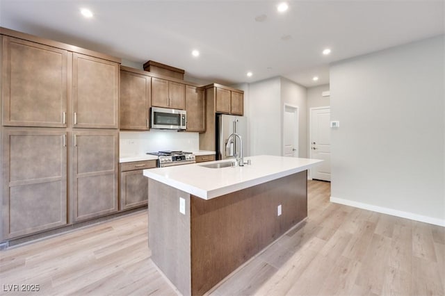 kitchen featuring appliances with stainless steel finishes, sink, a kitchen island with sink, and light wood-type flooring