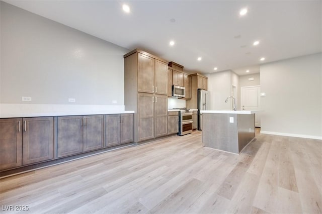 kitchen featuring stainless steel appliances, an island with sink, sink, and light hardwood / wood-style flooring