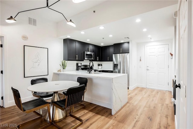 kitchen with appliances with stainless steel finishes, kitchen peninsula, sink, light stone counters, and light hardwood / wood-style floors