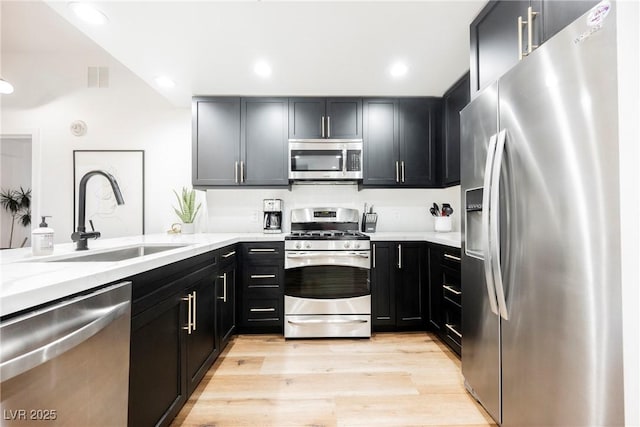 kitchen with appliances with stainless steel finishes, sink, light stone counters, and light hardwood / wood-style floors