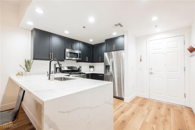 kitchen featuring appliances with stainless steel finishes, sink, light stone counters, kitchen peninsula, and light wood-type flooring