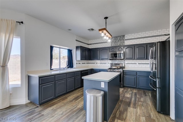 kitchen featuring appliances with stainless steel finishes, hanging light fixtures, dark hardwood / wood-style floors, a kitchen island, and decorative backsplash