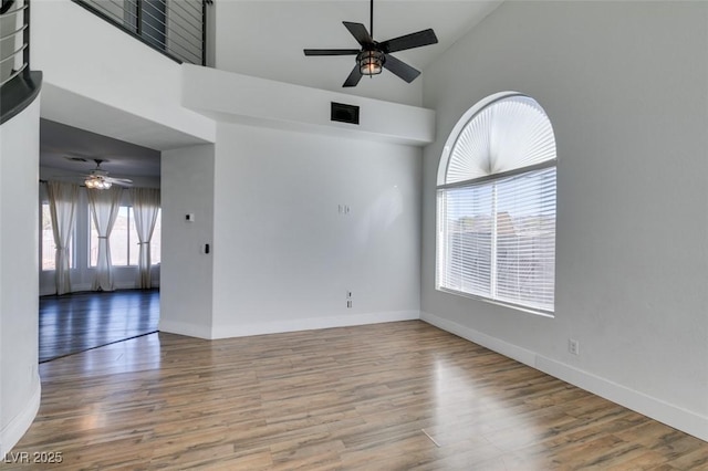 empty room featuring wood-type flooring, a towering ceiling, and ceiling fan