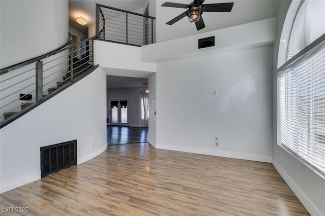 unfurnished living room featuring ceiling fan, light hardwood / wood-style flooring, and a towering ceiling