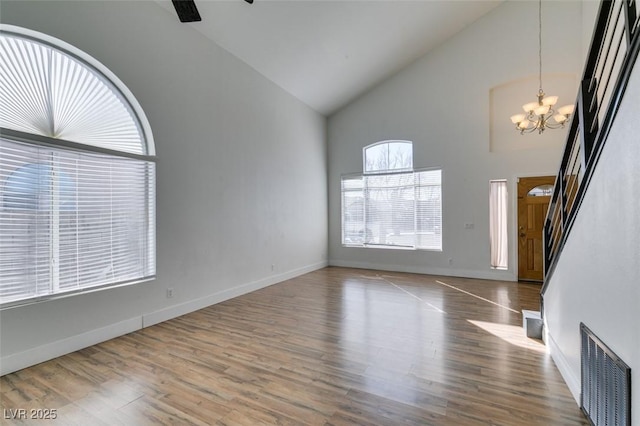 unfurnished living room featuring hardwood / wood-style flooring, ceiling fan with notable chandelier, and high vaulted ceiling