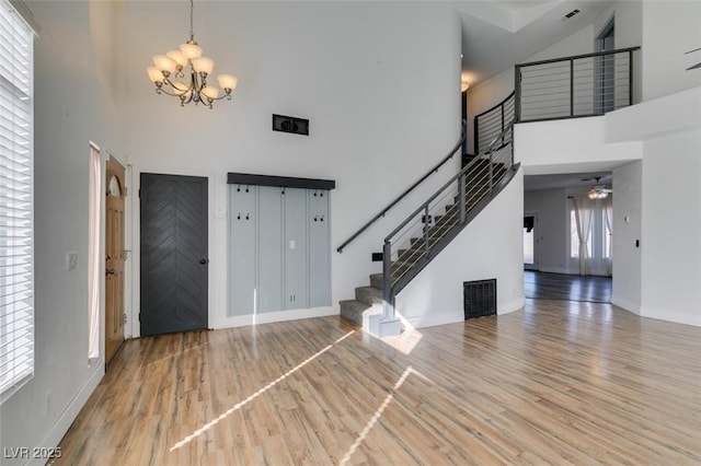 entryway featuring hardwood / wood-style flooring, ceiling fan with notable chandelier, and a high ceiling