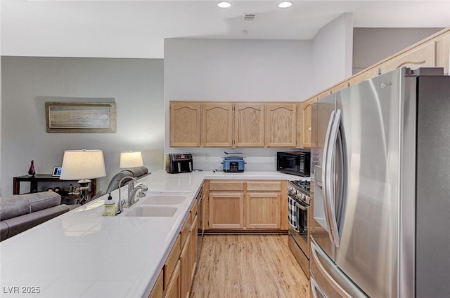 kitchen with appliances with stainless steel finishes, sink, light hardwood / wood-style floors, kitchen peninsula, and light brown cabinets