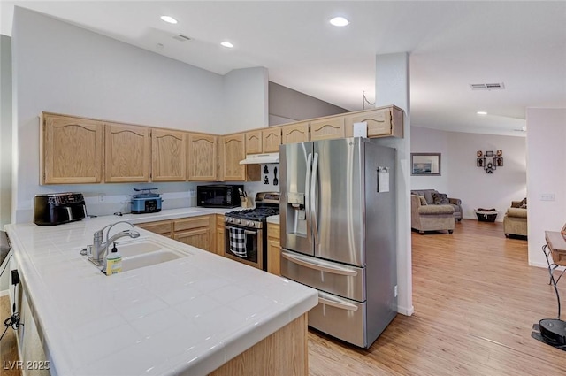 kitchen featuring sink, tile countertops, vaulted ceiling, light brown cabinets, and stainless steel appliances