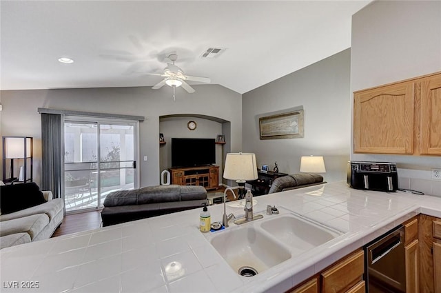 kitchen with lofted ceiling, sink, dishwasher, ceiling fan, and tile counters