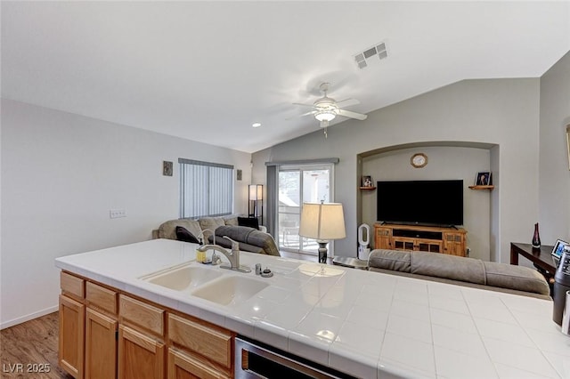 kitchen with tile countertops, lofted ceiling, sink, dishwashing machine, and light hardwood / wood-style flooring