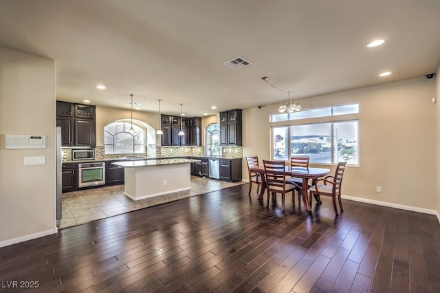 kitchen with hanging light fixtures, stainless steel appliances, a center island, dark brown cabinetry, and decorative backsplash