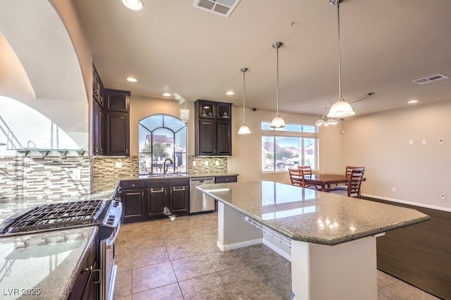 kitchen featuring a breakfast bar area, appliances with stainless steel finishes, dark brown cabinets, a center island, and light stone countertops