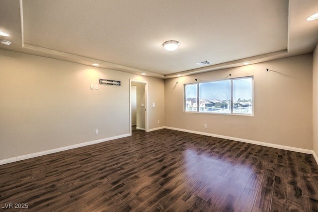 unfurnished room featuring dark wood-type flooring and a tray ceiling