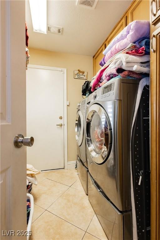 laundry area featuring cabinet space, washing machine and dryer, light tile patterned floors, and visible vents