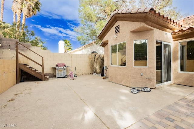 view of side of home with stucco siding, a patio area, a tile roof, and fence