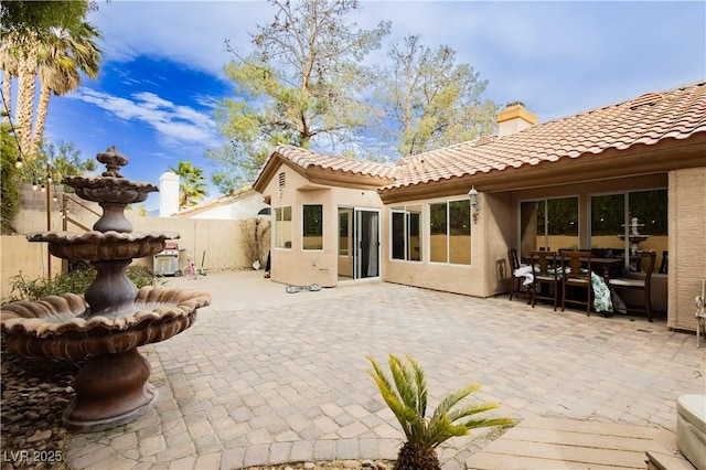 rear view of property featuring stucco siding, a tiled roof, fence, and a patio