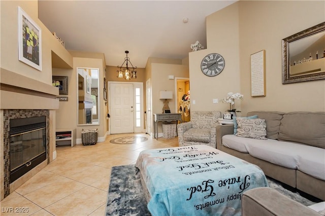 living area with light tile patterned floors, a tiled fireplace, baseboards, and a notable chandelier