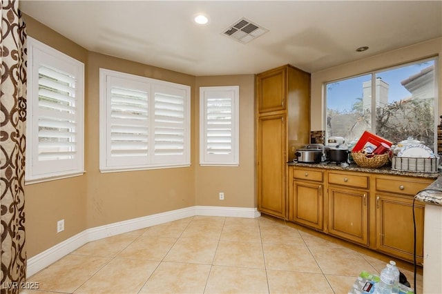 kitchen featuring light tile patterned floors, dark stone countertops, visible vents, and brown cabinets