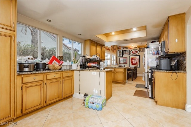 kitchen featuring a peninsula, light stone countertops, a tray ceiling, and stainless steel microwave