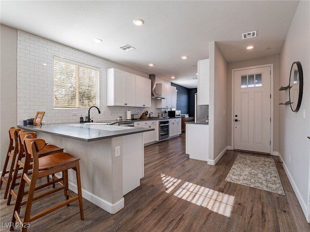 kitchen with a kitchen breakfast bar, white cabinets, decorative backsplash, kitchen peninsula, and wall chimney exhaust hood