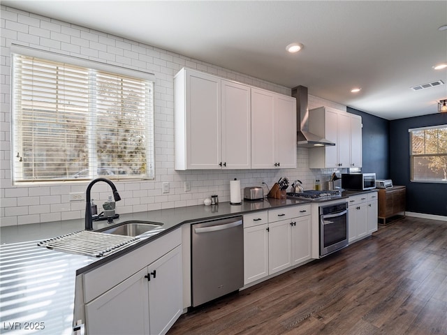 kitchen featuring wall chimney range hood, dark wood-type flooring, appliances with stainless steel finishes, tasteful backsplash, and white cabinets