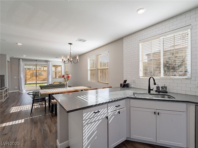 kitchen with decorative light fixtures, sink, white cabinets, dark hardwood / wood-style flooring, and kitchen peninsula