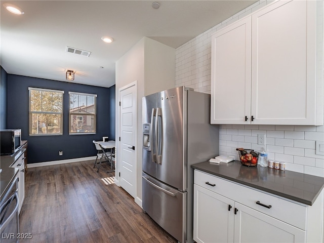 kitchen with appliances with stainless steel finishes, dark hardwood / wood-style floors, white cabinets, and backsplash