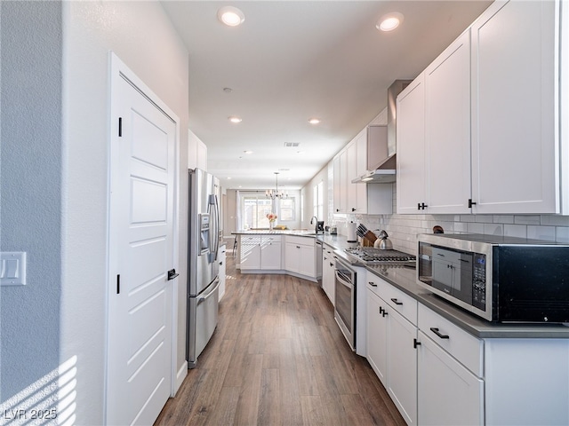 kitchen with appliances with stainless steel finishes, tasteful backsplash, wood-type flooring, white cabinets, and kitchen peninsula