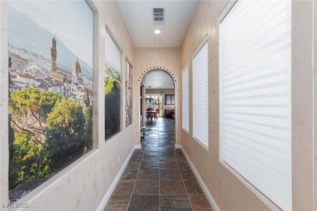 corridor featuring baseboards, arched walkways, visible vents, and stone tile flooring