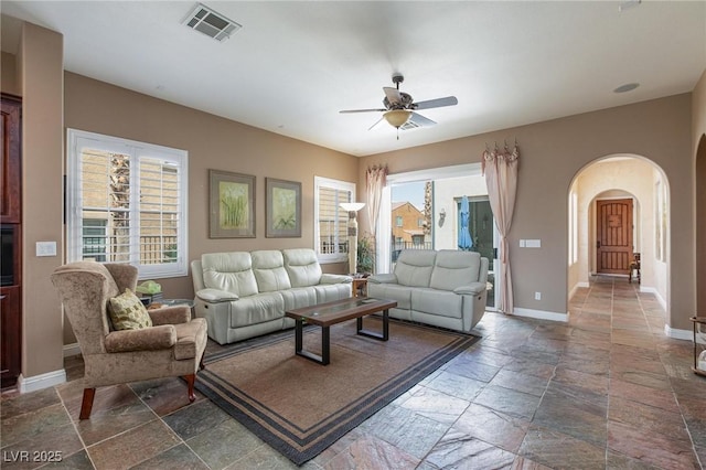 living room with visible vents, ceiling fan, baseboards, arched walkways, and stone tile flooring