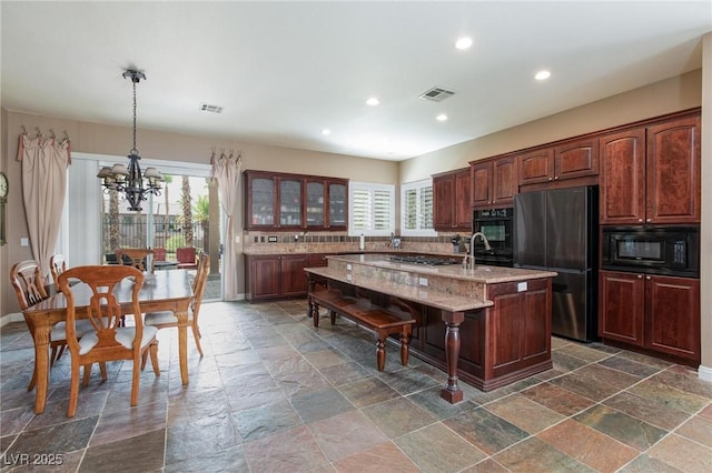 kitchen with stone tile flooring, visible vents, black appliances, and an island with sink