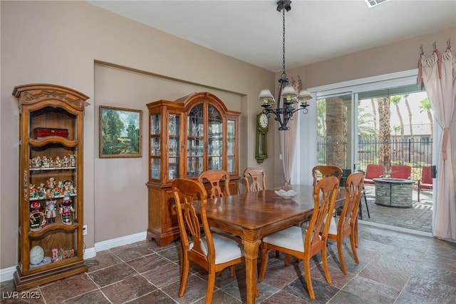 dining room with stone tile floors, a notable chandelier, and baseboards