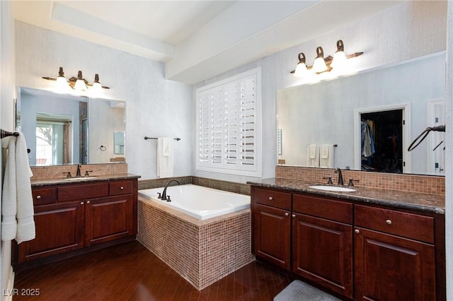 bathroom with vanity, hardwood / wood-style floors, backsplash, and a relaxing tiled tub