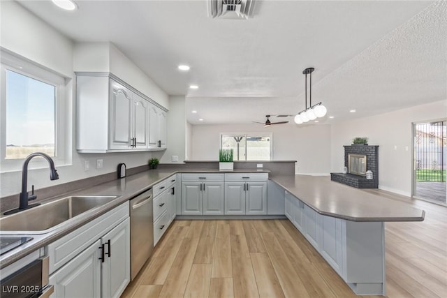 kitchen with pendant lighting, sink, dishwasher, a fireplace, and kitchen peninsula