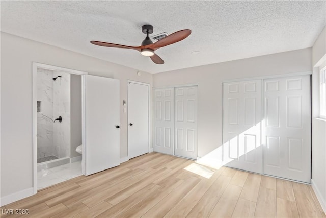 unfurnished bedroom featuring ensuite bath, a textured ceiling, light hardwood / wood-style flooring, two closets, and ceiling fan