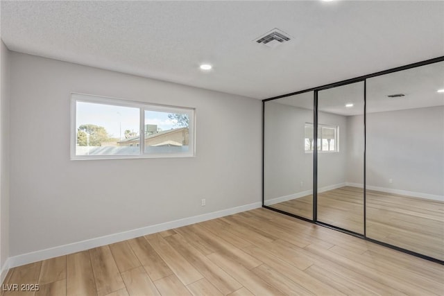 unfurnished bedroom with multiple windows, light hardwood / wood-style flooring, a closet, and a textured ceiling