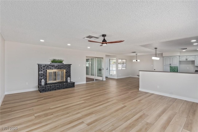 unfurnished living room featuring a brick fireplace, a textured ceiling, ceiling fan, and light wood-type flooring