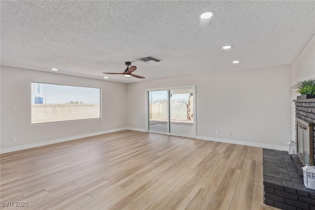 unfurnished living room with ceiling fan, a fireplace, light hardwood / wood-style flooring, and a textured ceiling