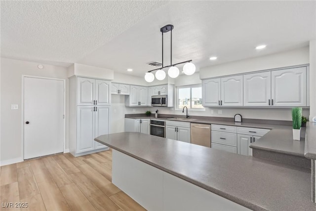 kitchen with pendant lighting, light hardwood / wood-style flooring, white cabinets, and appliances with stainless steel finishes