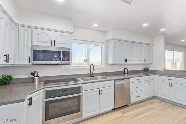 kitchen with appliances with stainless steel finishes, a wealth of natural light, sink, and white cabinets