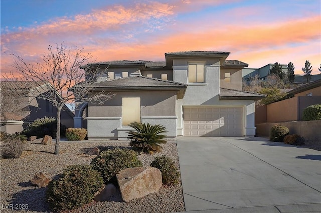 prairie-style home with fence, driveway, an attached garage, stucco siding, and a tiled roof