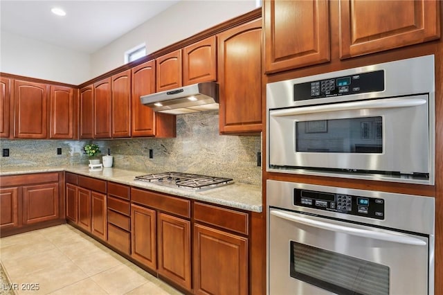 kitchen featuring light stone counters, light tile patterned floors, stainless steel appliances, decorative backsplash, and under cabinet range hood